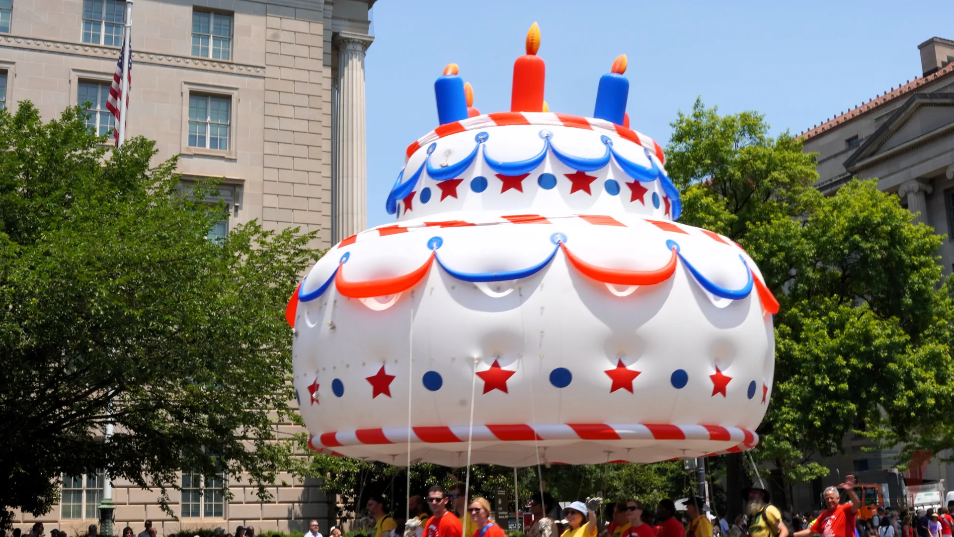 A large inflatable cake float with candles and decorations at a parade.