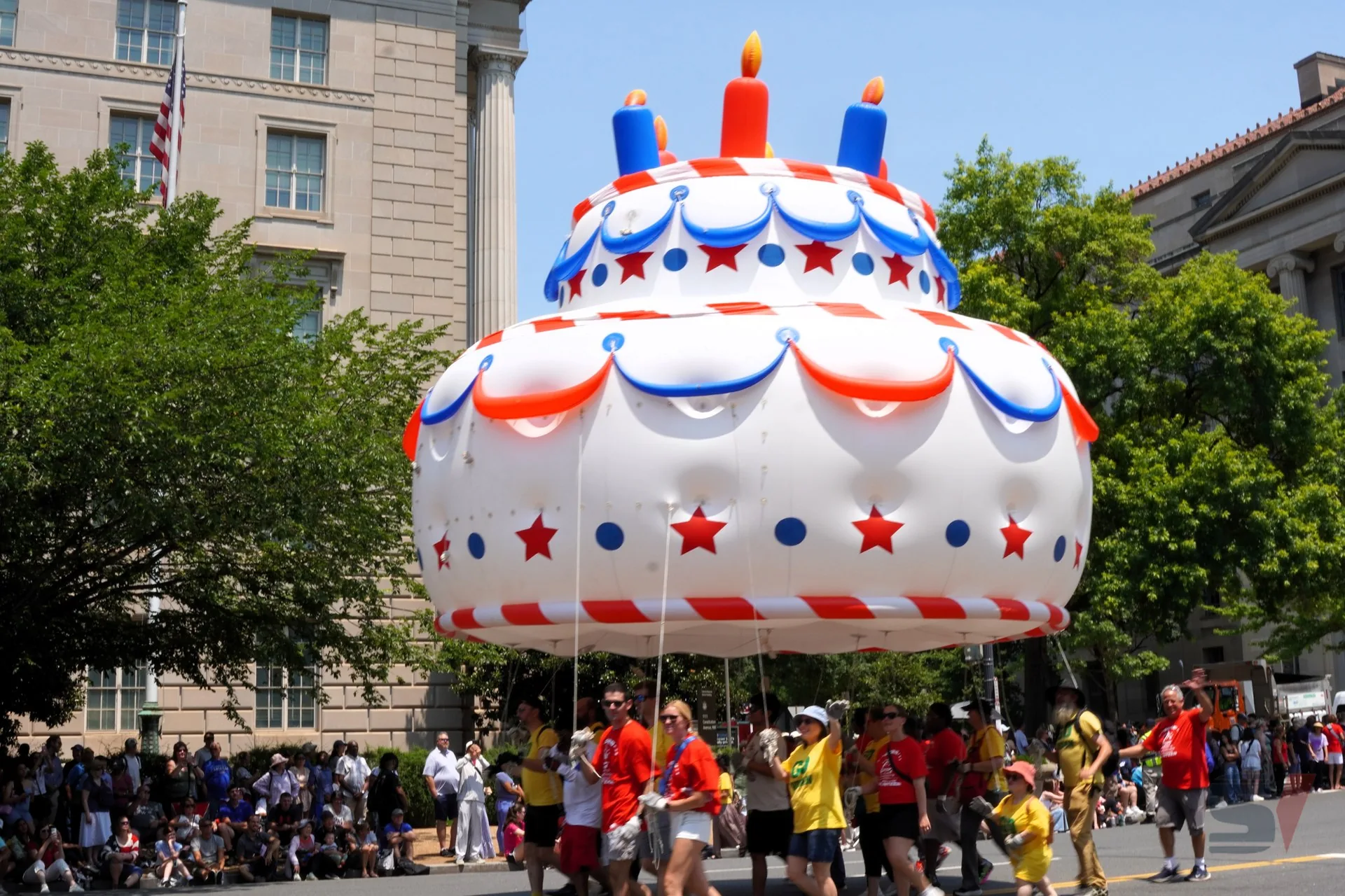 A large inflatable cake float with candles and decorations at a parade.
