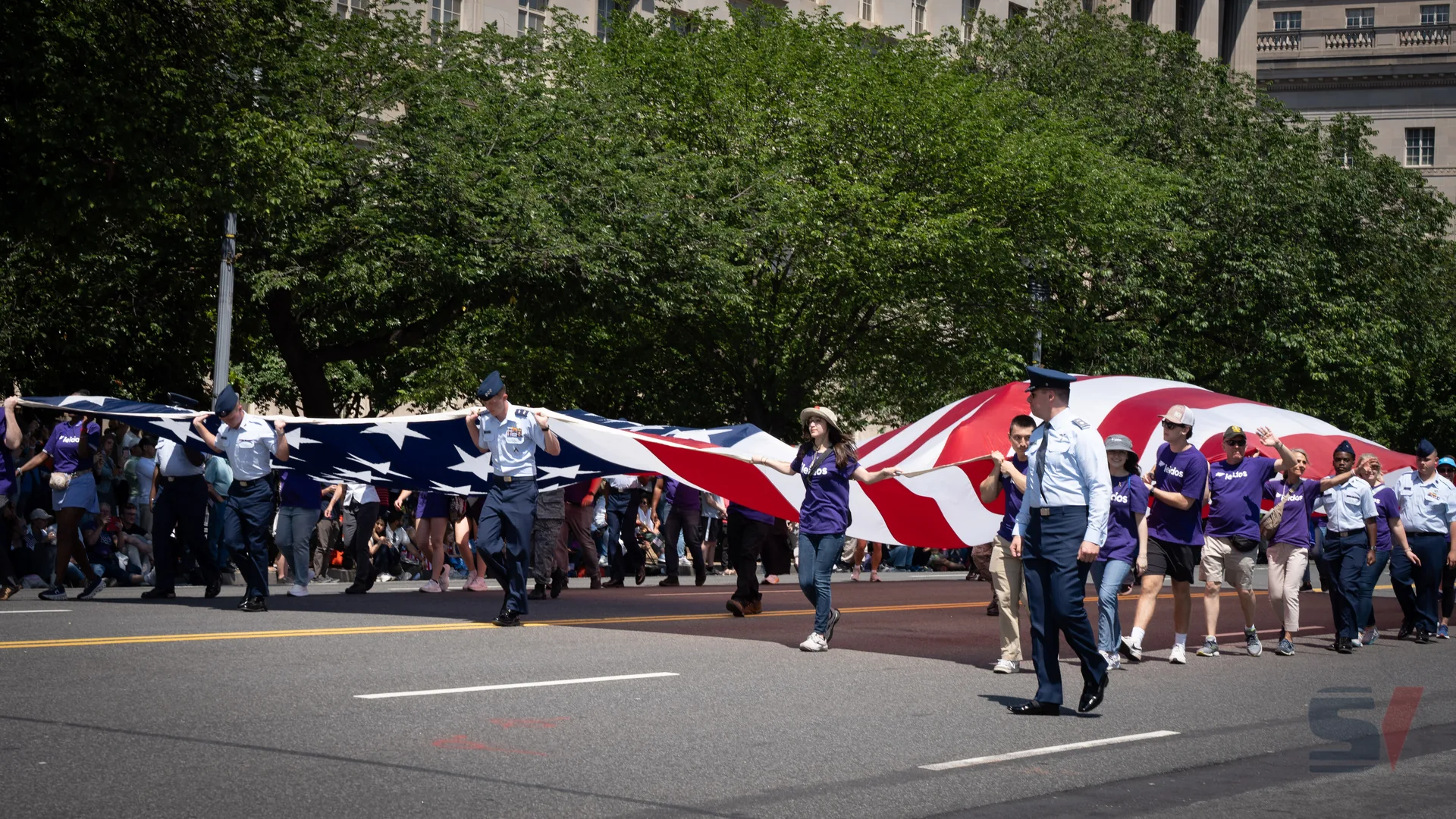 Participants in the National Memorial Day Parade carry a large American flag along the street.