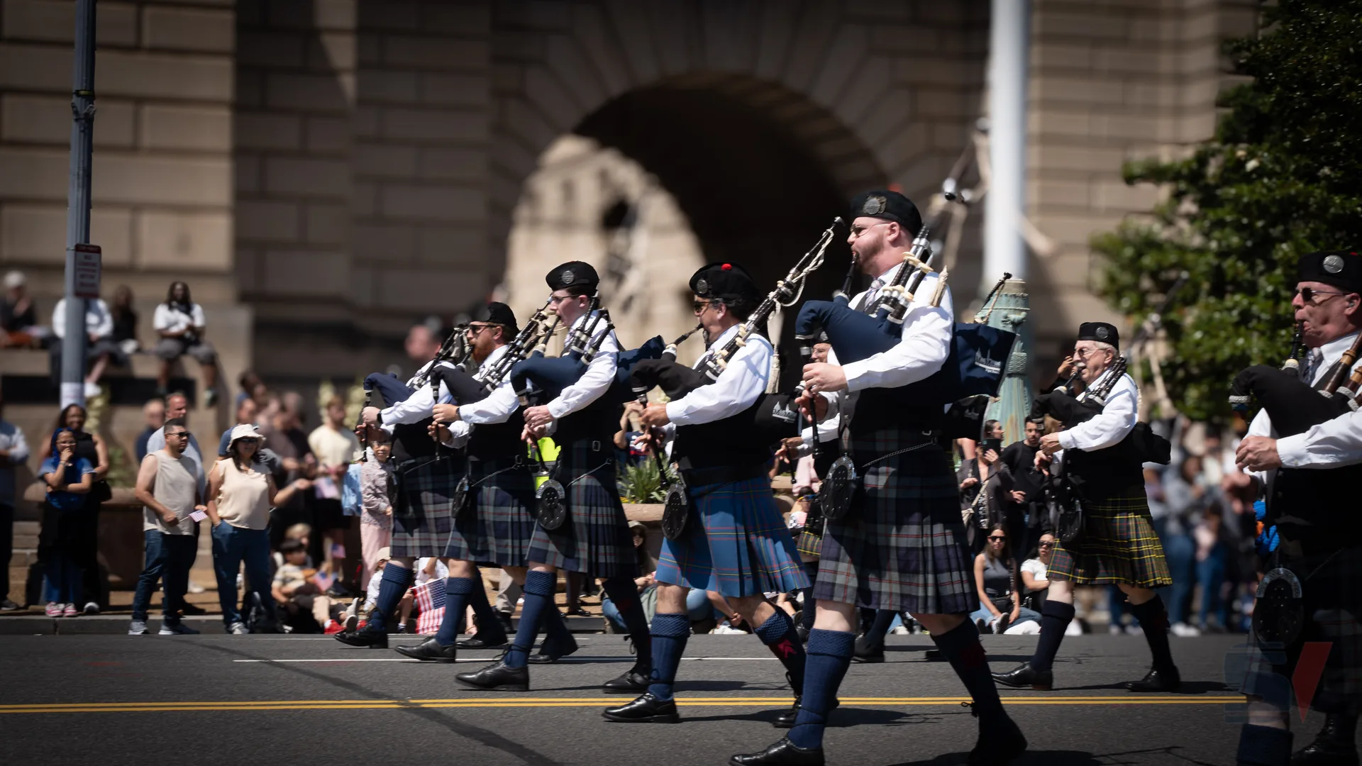 A group of bagpipers dressed in traditional Scottish attire performs during a parade.