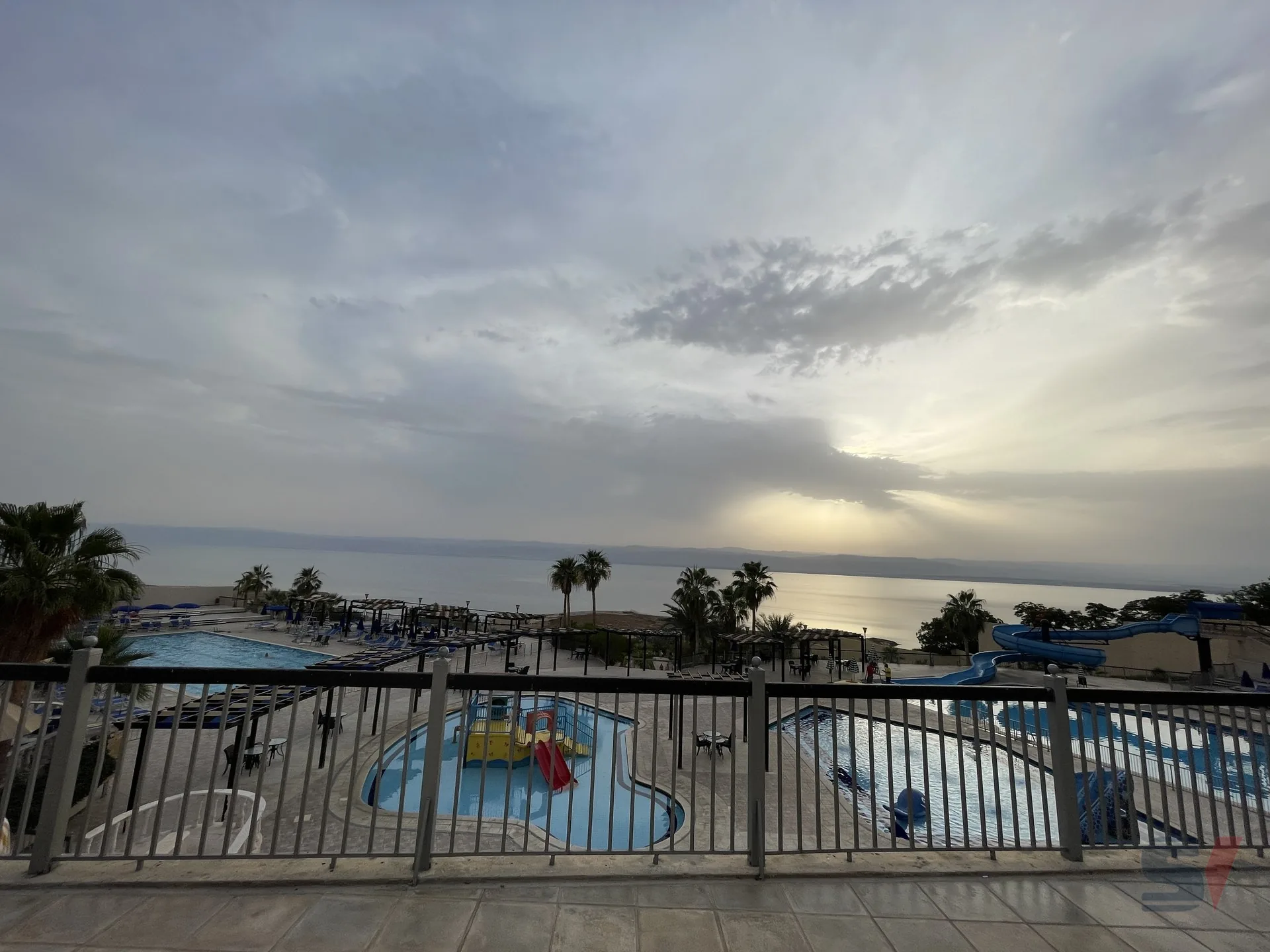A serene view of pools and the Dead Sea at sunset.