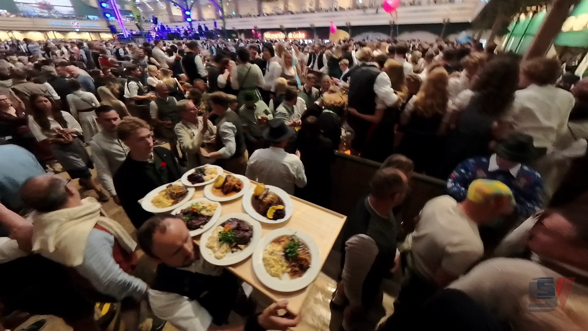 A server carrying platters of traditional Bavarian dishes amidst a crowd at Oktoberfest.