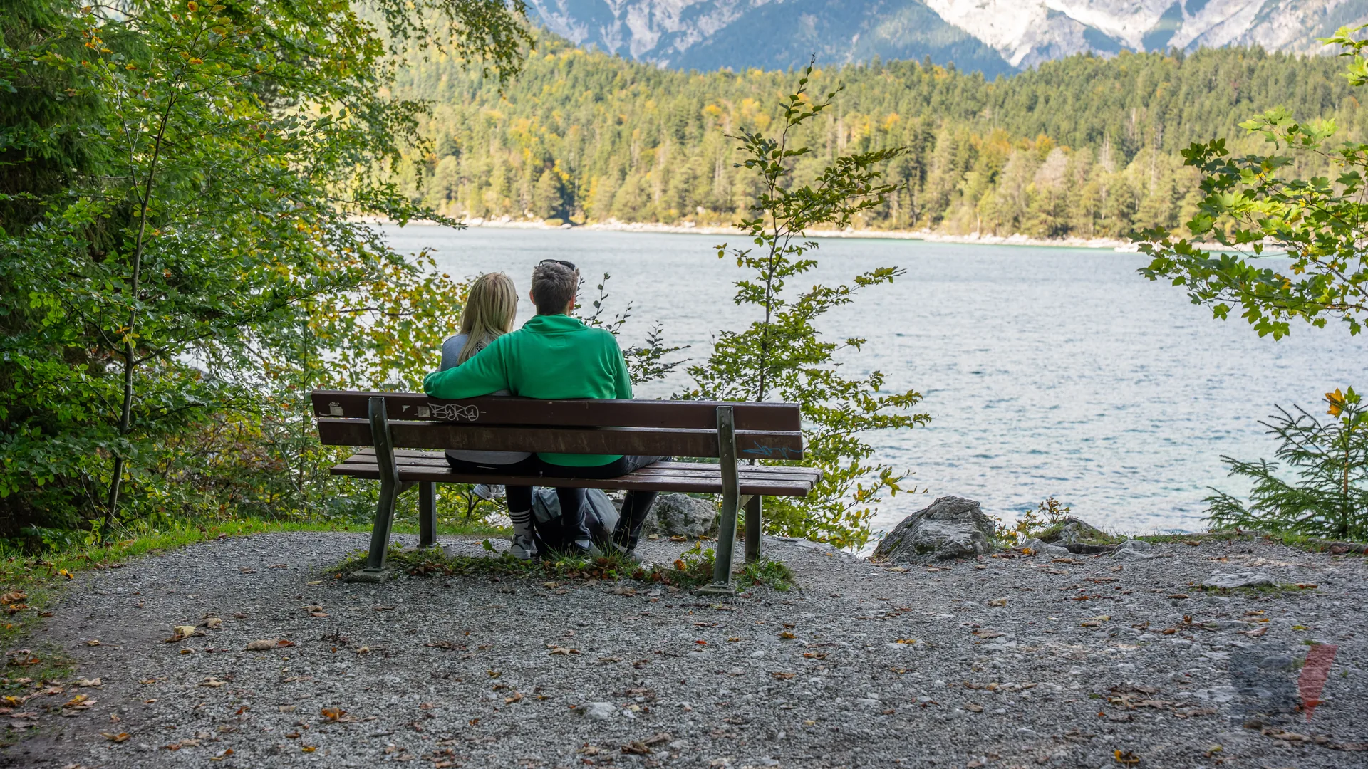 A couple sitting on a bench overlooking Eibsee Lake with mountains in the background.