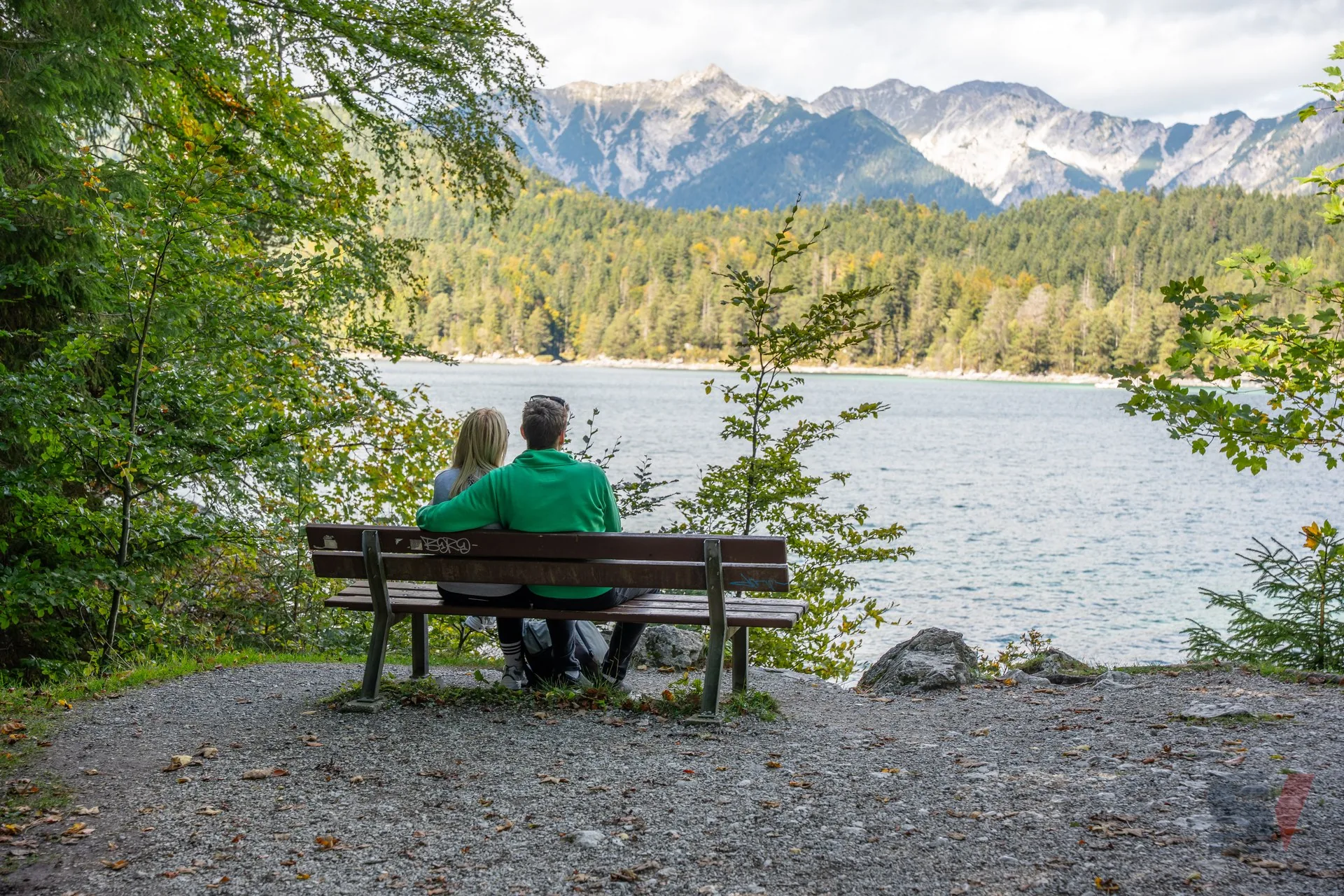 Ein Paar sitzt auf einer Bank mit Blick auf den Eibsee und die Berge im Hintergrund.