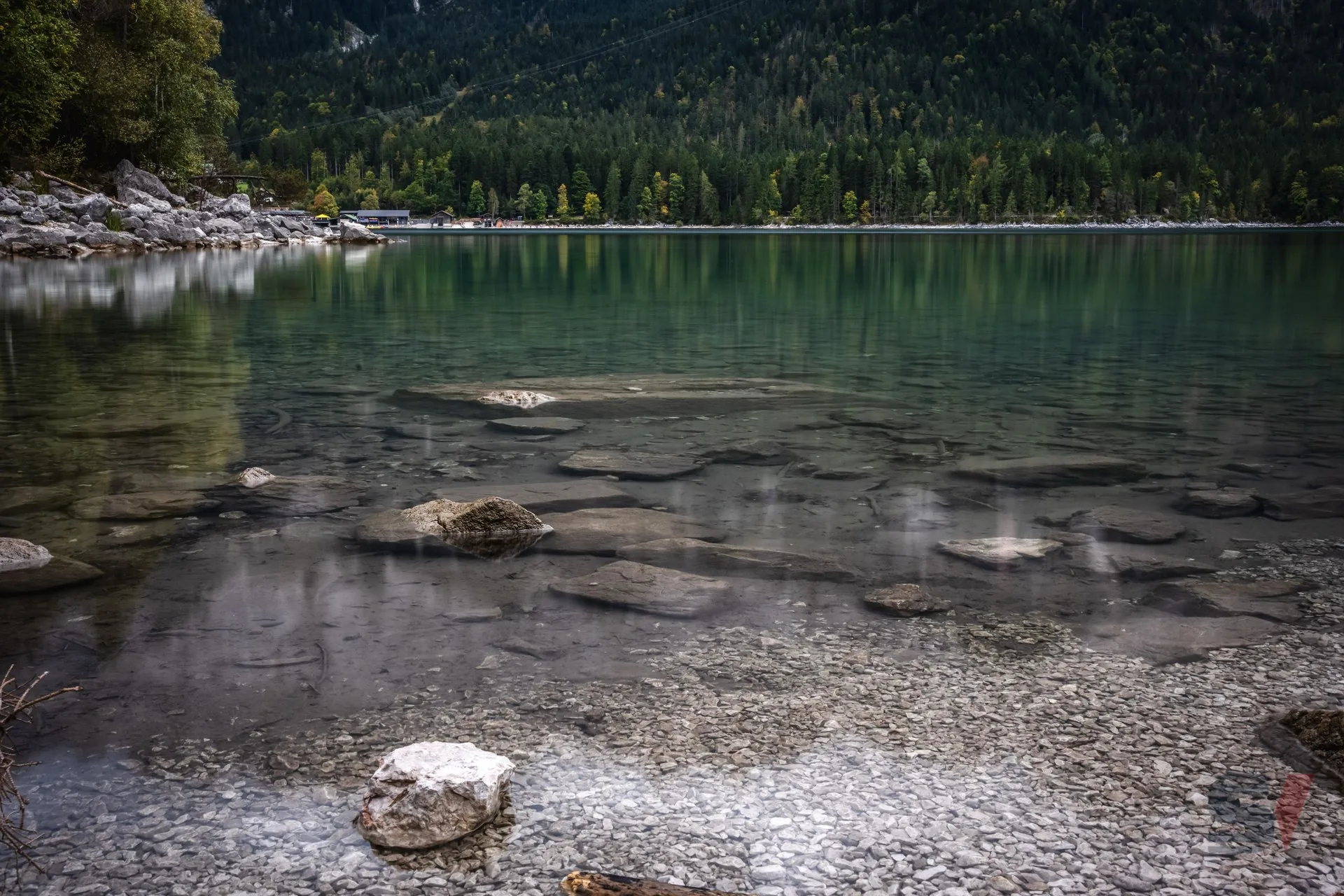 Kristallklares, türkisfarbenes Wasser des Eibsee mit sichtbaren Steinen und Spiegelungen.