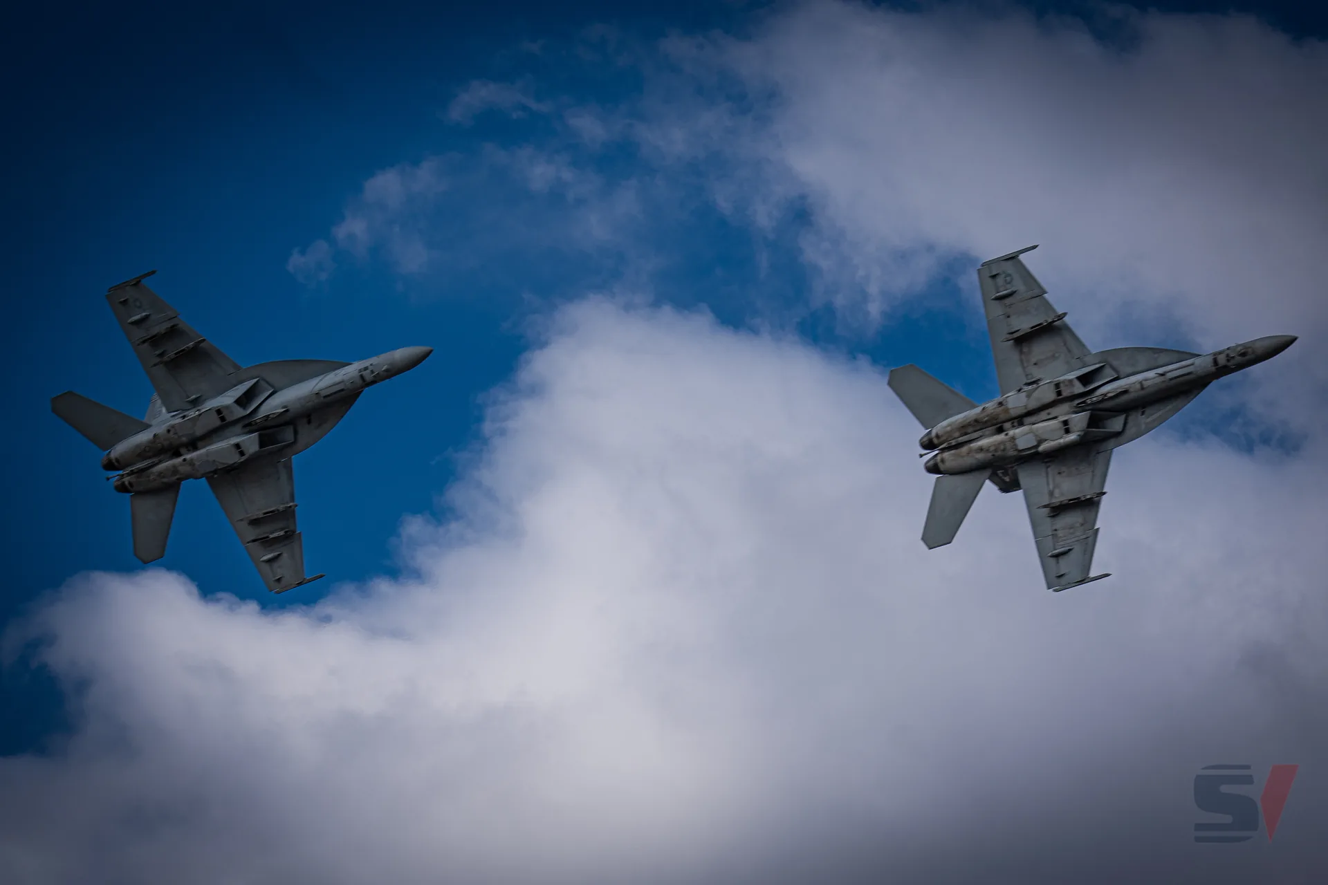 Two fighter jets soaring through a blue sky with clouds.