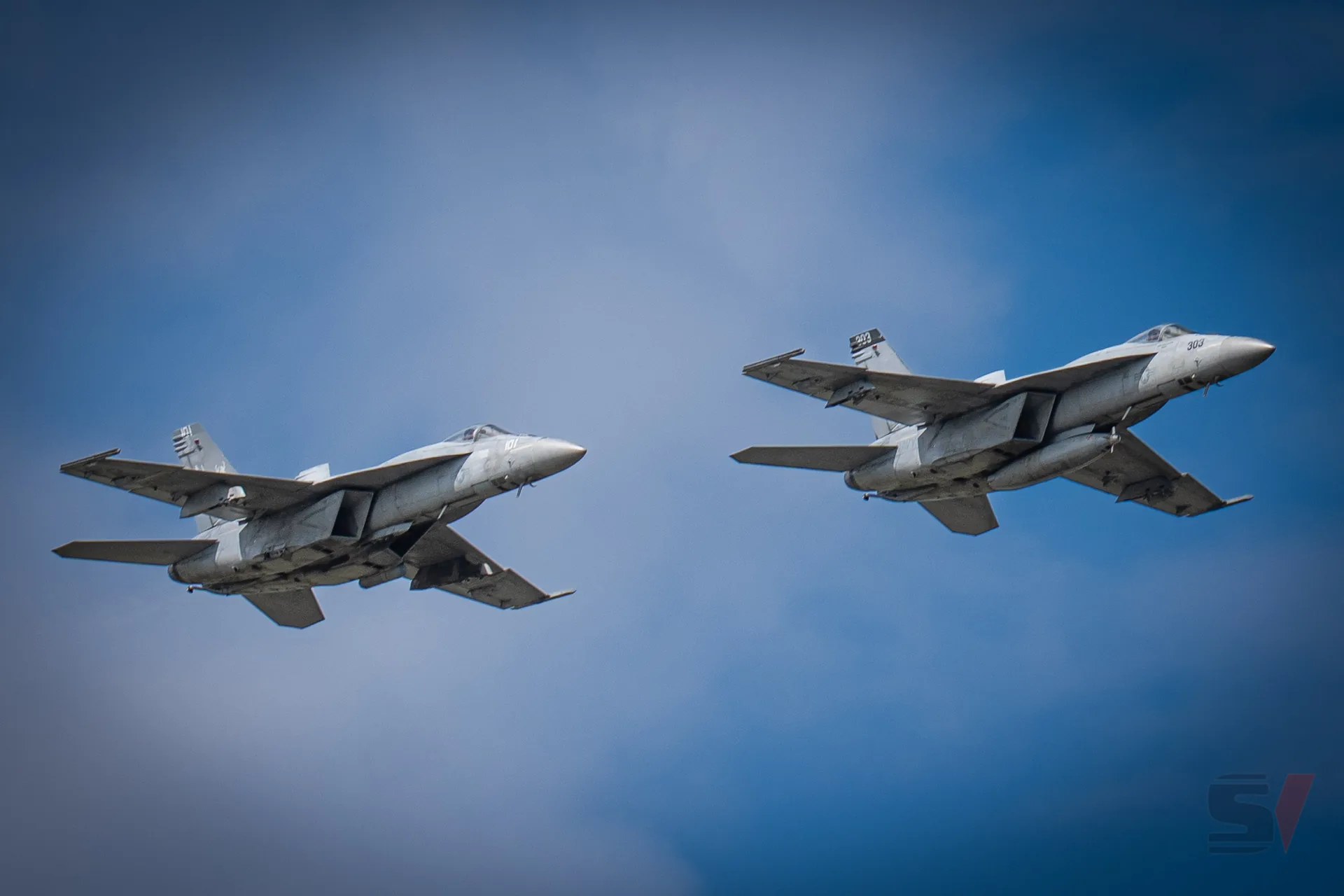 Two F/A-18 Hornet fighter jets flying in formation against a blue sky.