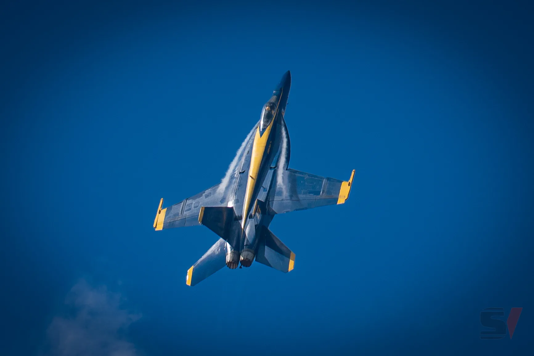 A Blue Angels jet performs a vertical climb against a clear blue sky.