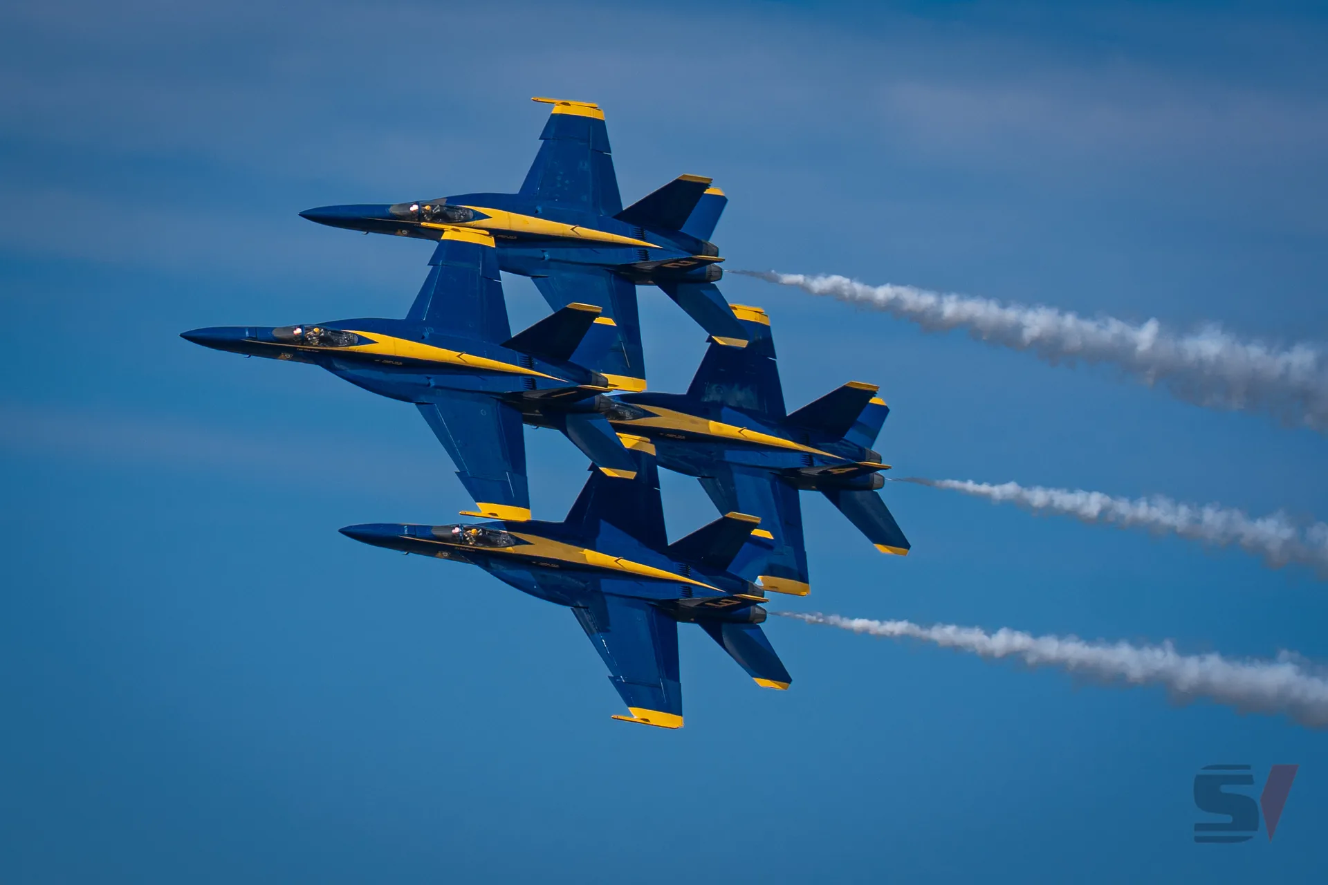 Four Blue Angels jets flying in a tight formation with vapor trails.
