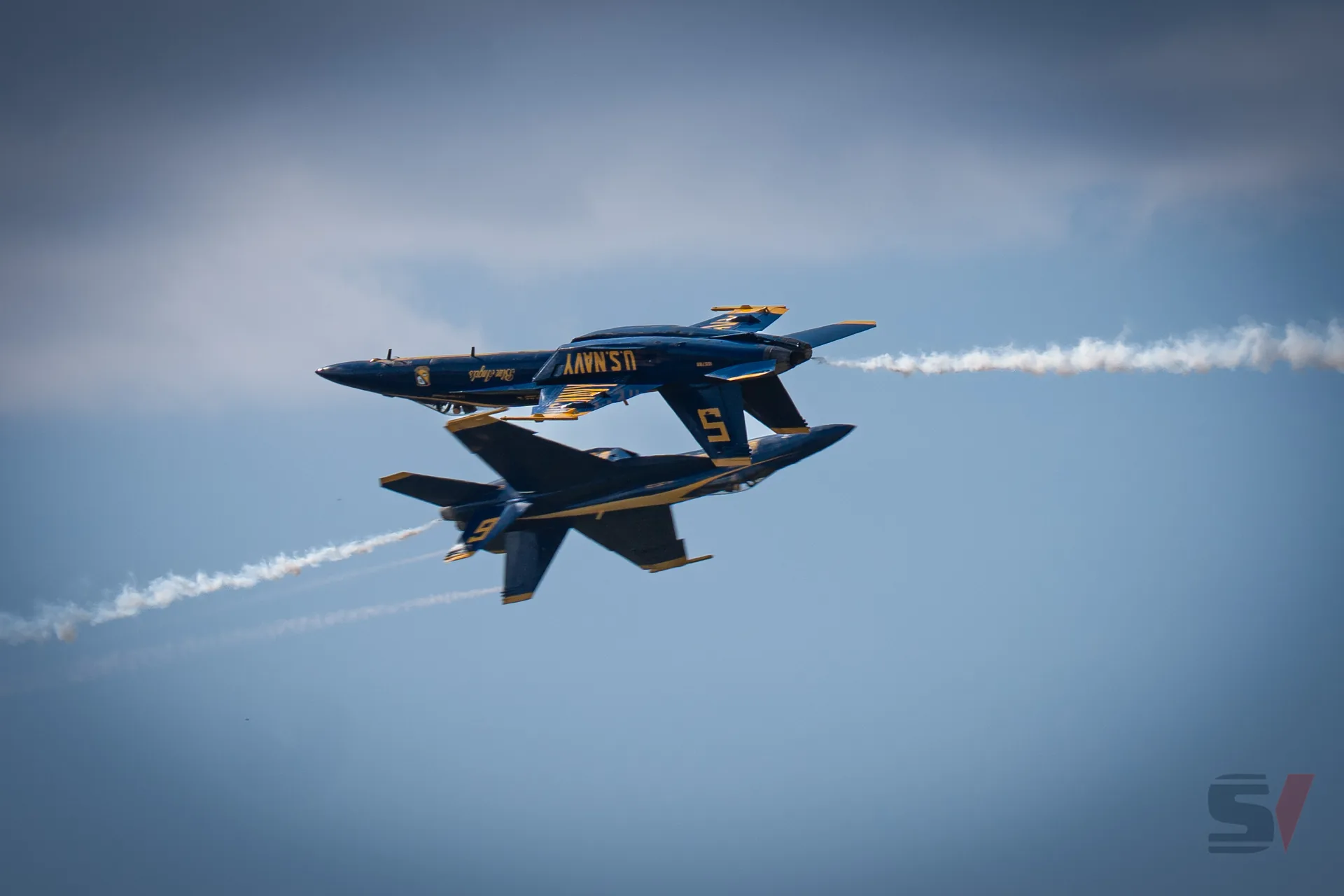 Two Blue Angels jets performing a close aerial maneuver with smoke trails.