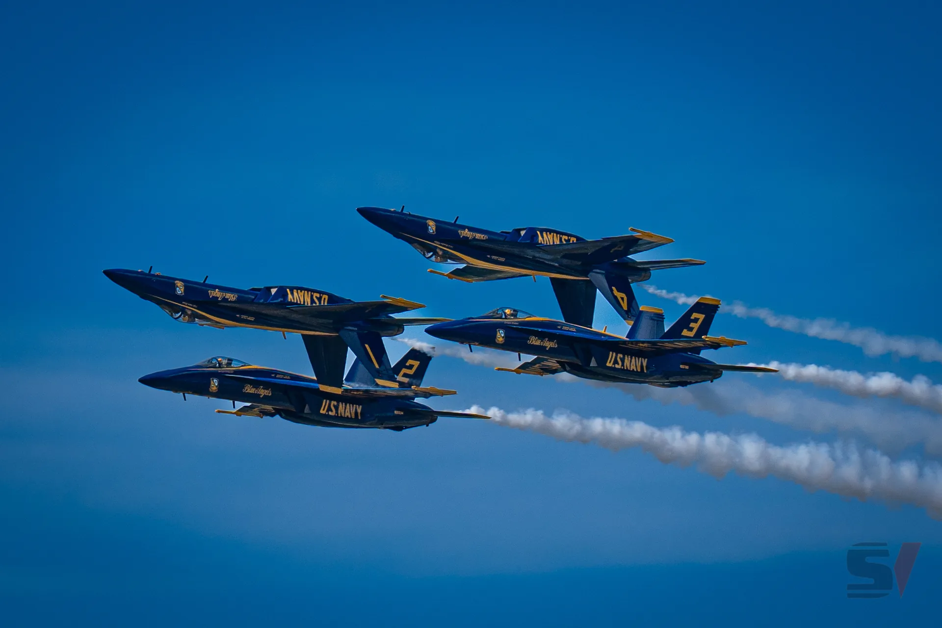 Four Blue Angels F/A-18 Hornets flying in tight formation with smoke trails.
