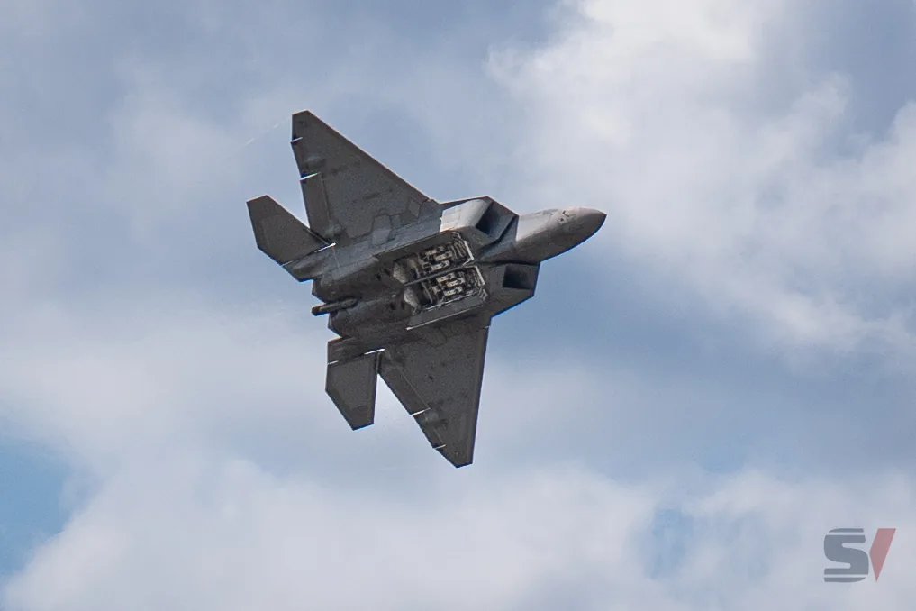 F-22 Raptor flying upside down against a cloudy sky.