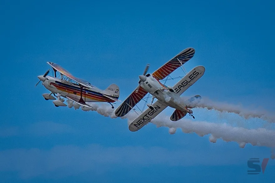 Two biplanes execute a daring aerial maneuver with smoke trails.