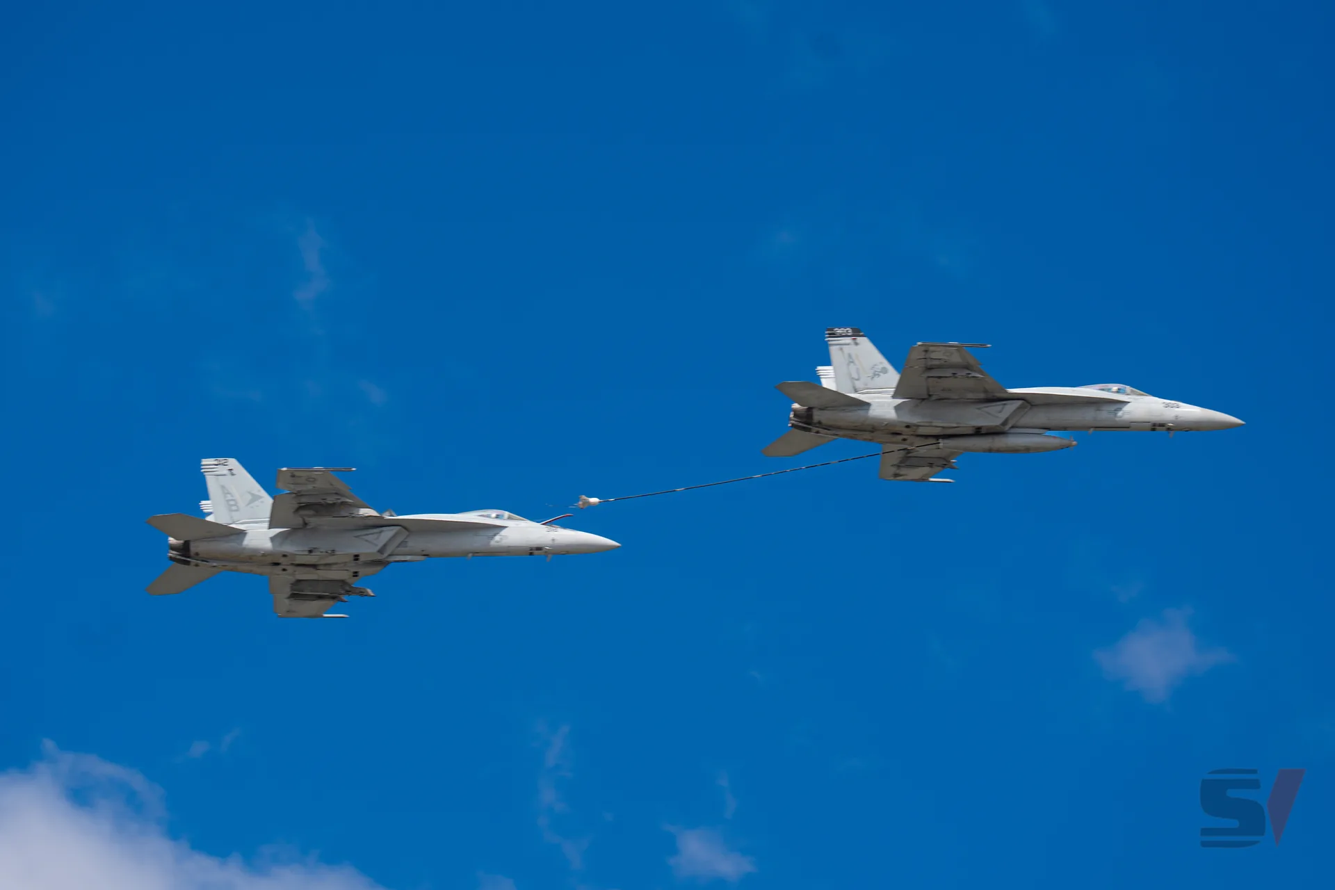 Two fighter jets engaged in mid-air refueling against a clear blue sky.