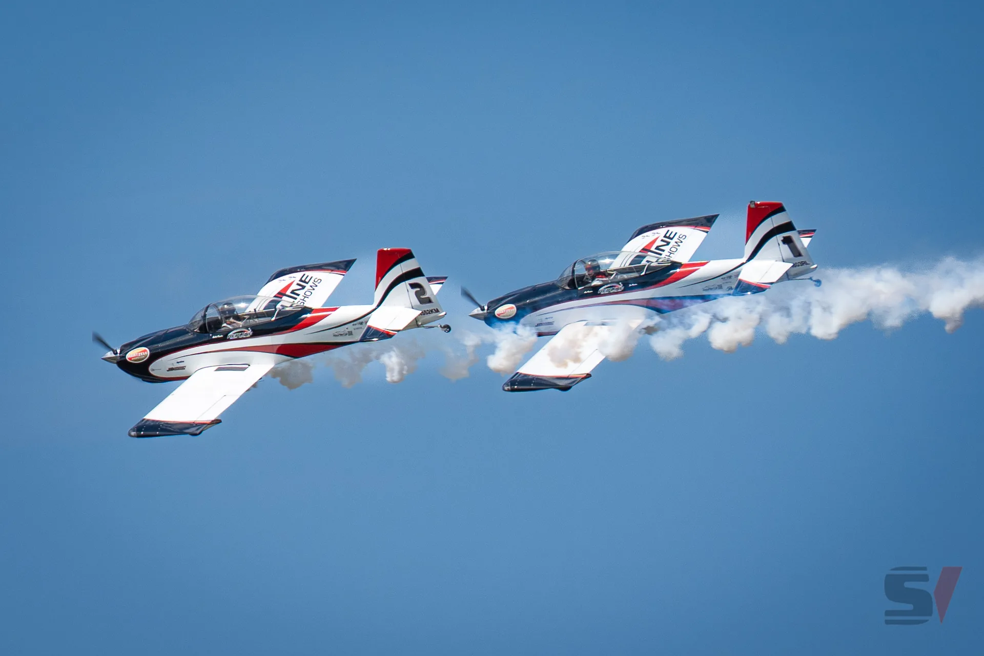 Two aerobatic planes performing synchronized maneuvers with smoke trails.