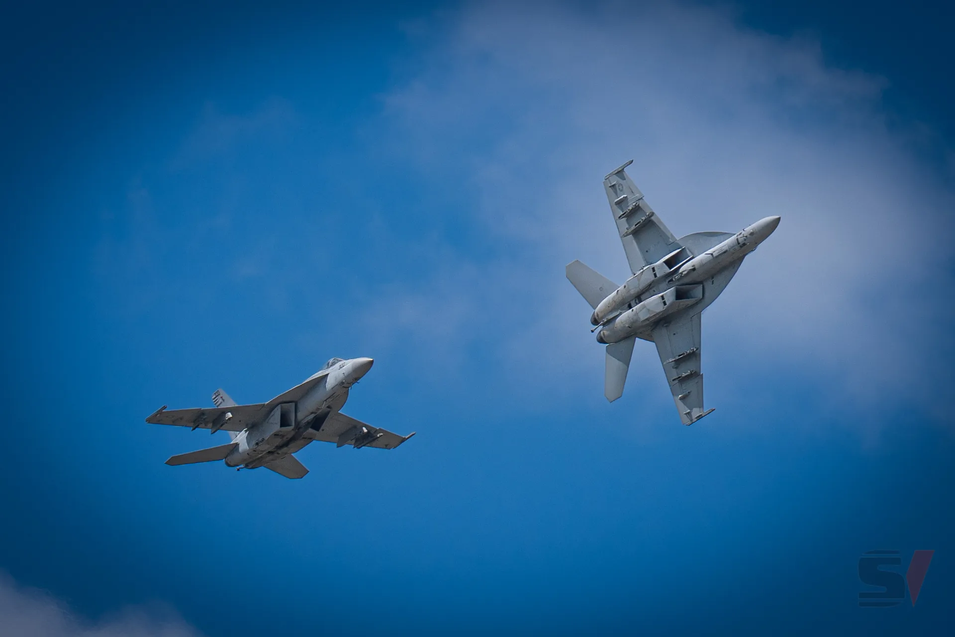 Two F/A-18 Hornets performing a synchronized maneuver in the sky.