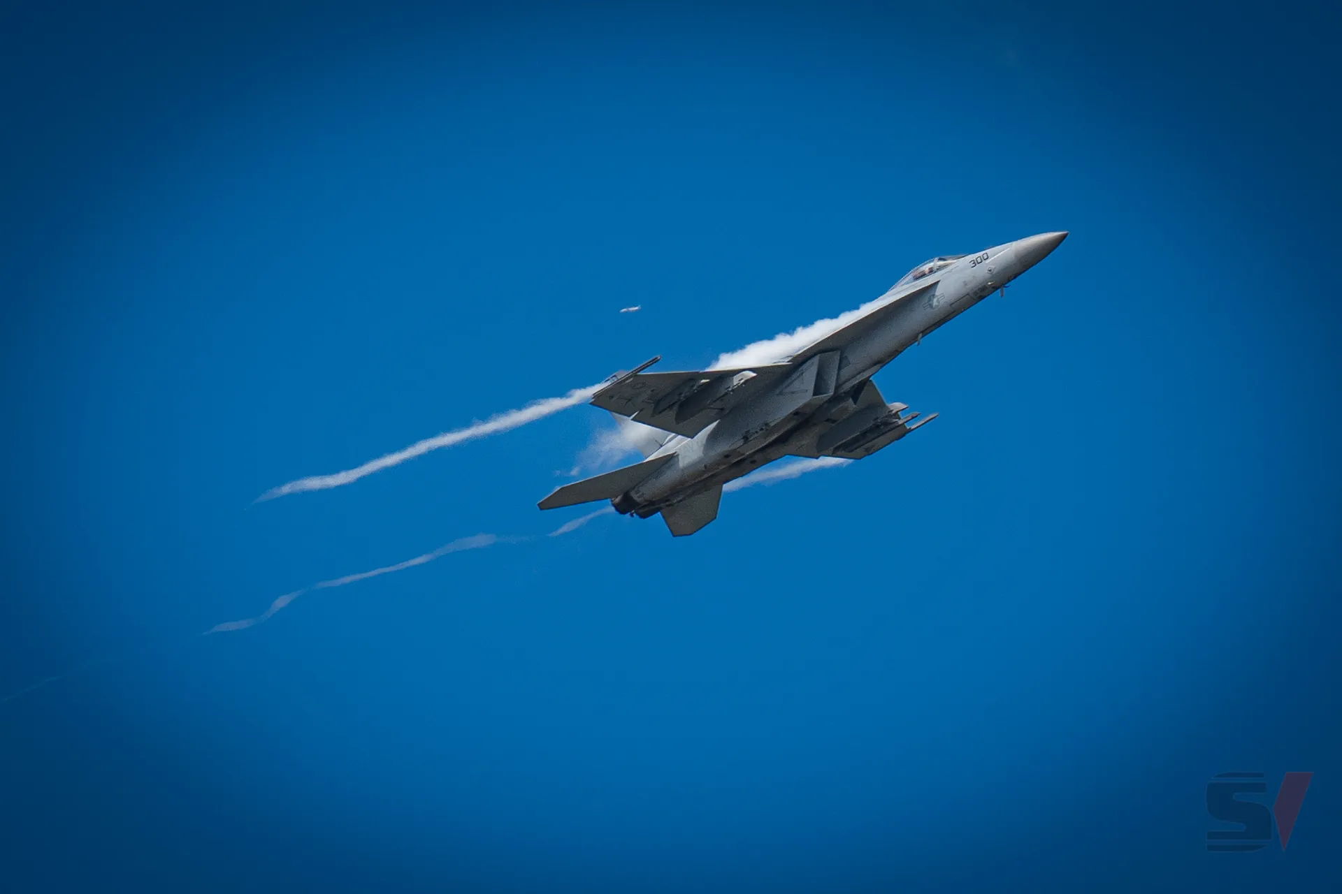 Fighter jet performing a steep climb with contrails against a blue sky.