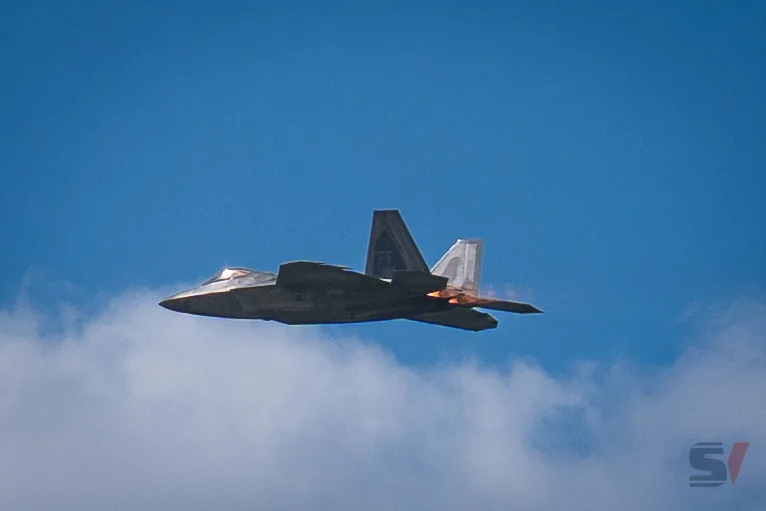 F-22 Raptor jet flying against a blue sky with clouds.