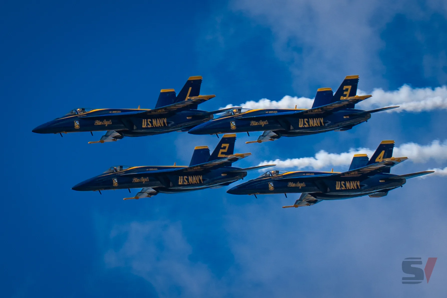 Four Blue Angels jets flying in formation against a blue sky.