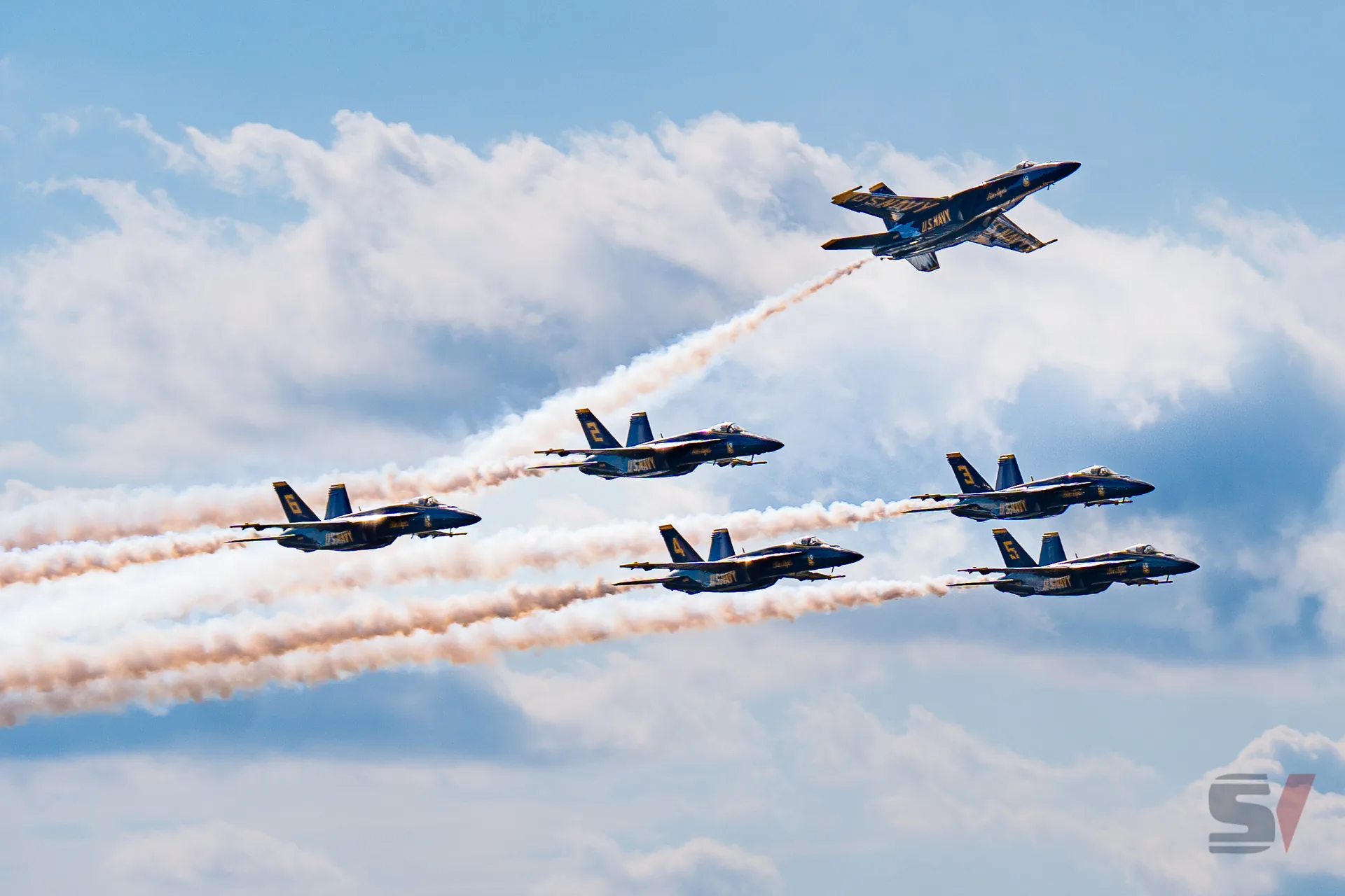 Six Blue Angels jets performing a formation flight with smoke trails.