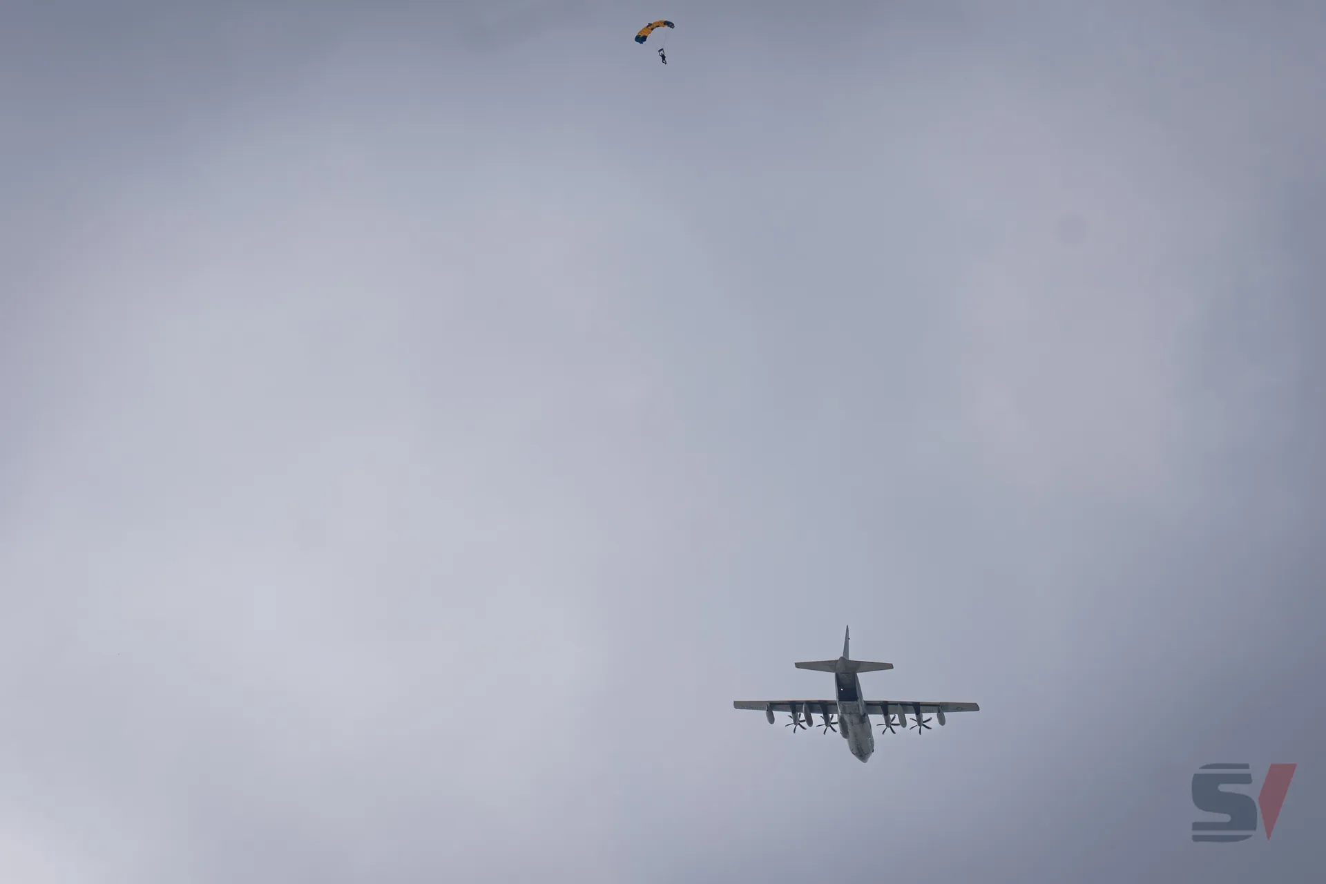 A parachutist descends beneath a brightly colored parachute from a C-130 aircraft.