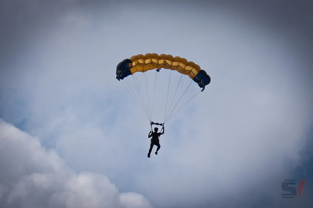 A solo parachutist descends with a yellow and blue parachute at NAS Oceana Air Show.