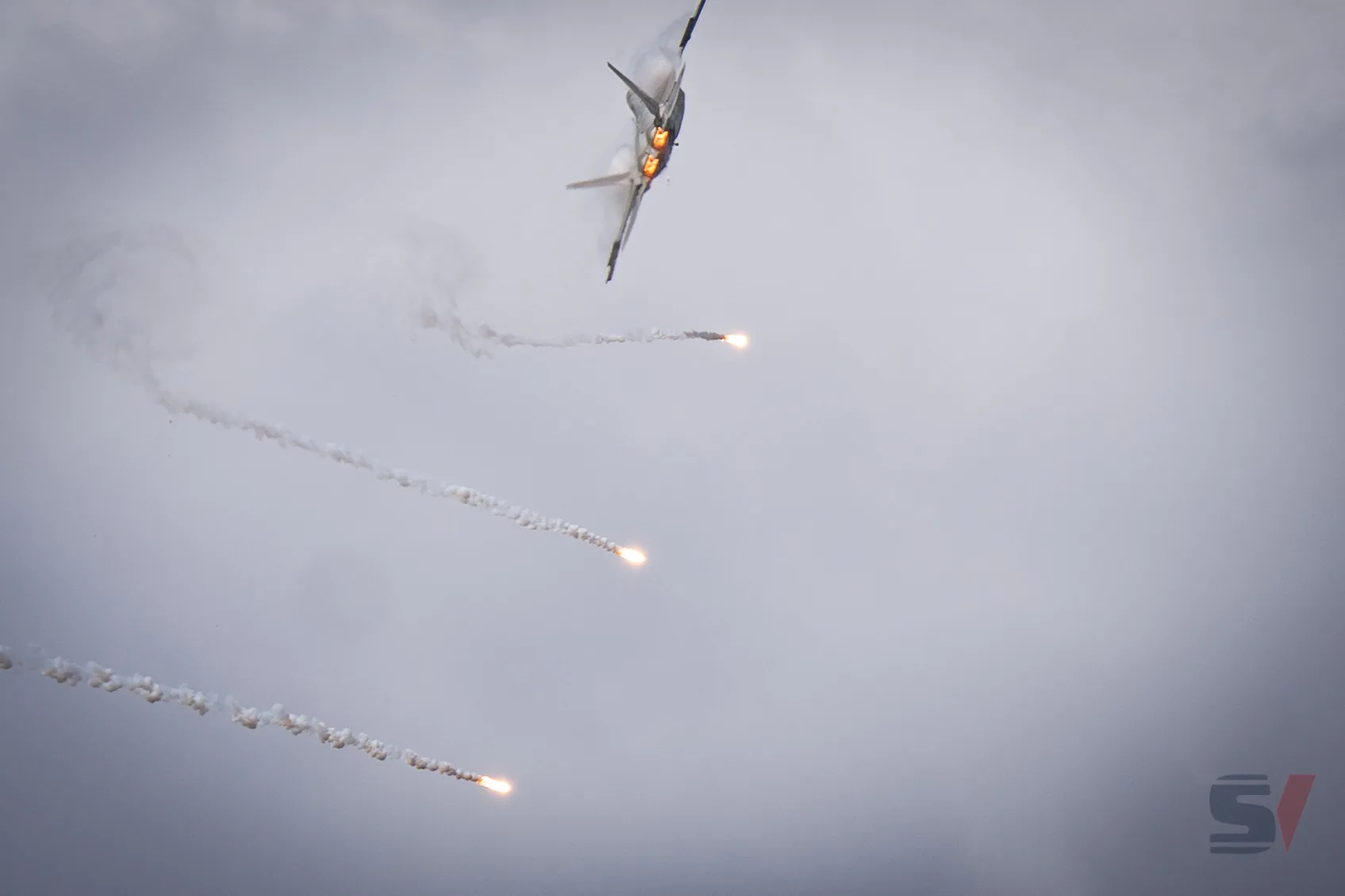 A fighter jet performs a dramatic maneuver, releasing flares in the sky.