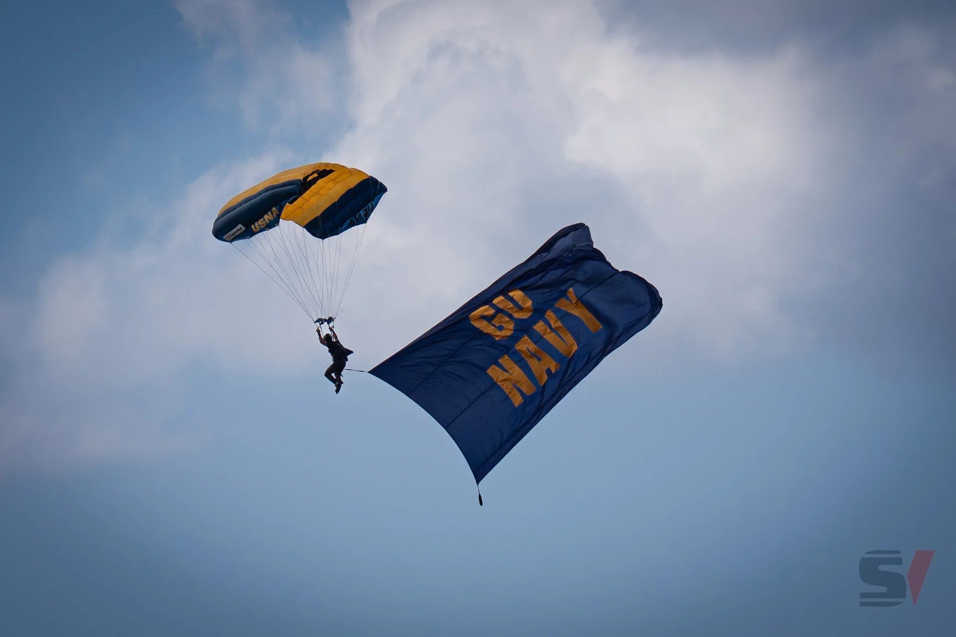 A parachutist descending with a large 'GO NAVY' flag at the air show.